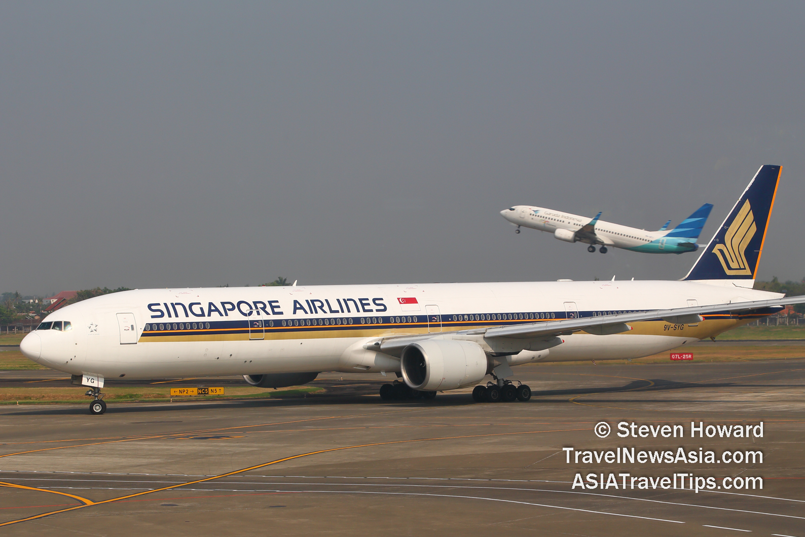 Singapore Airlines Boeing 777 reg: 9V-SYG in the foreground with a Garuda aircraft taking off in the background. Picture by Steven Howard of TravelNewsAsia.com Click to enlarge.