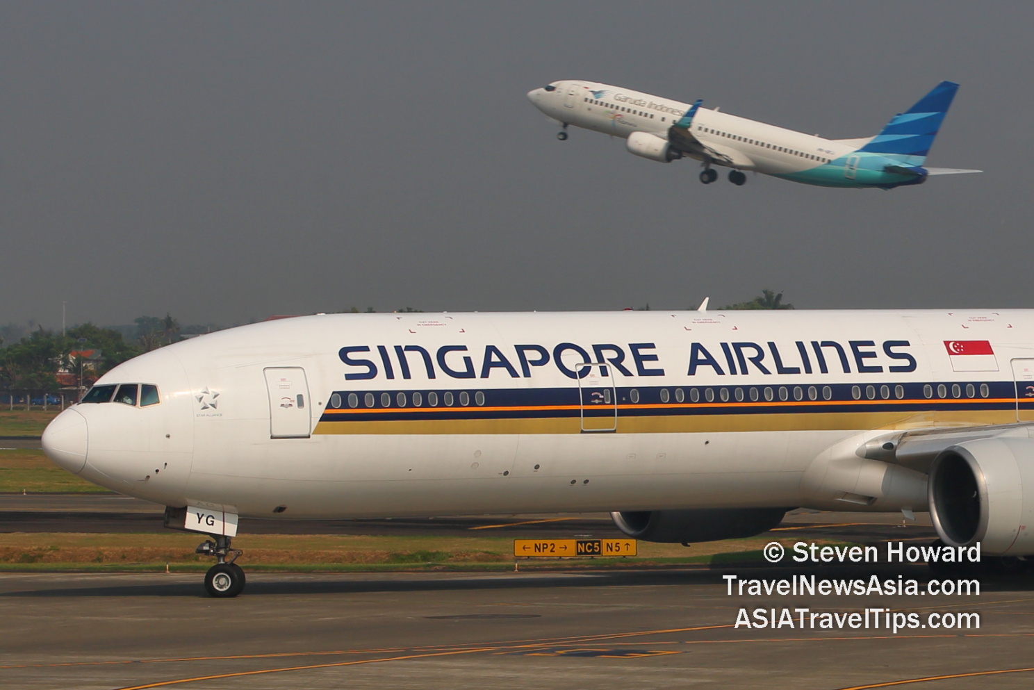 Singapore Airlines Boeing 777 reg: 9V-SYG in the foreground, with a Garuda aircraft taking off in the background. Picture by Steven Howard of TravelNewsAsia.com Click to enlarge.