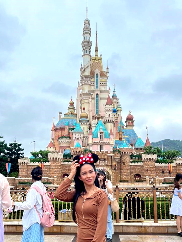 Tourist from Thailand poses in front of reimagined Castle of Magical Dreams at Hong Kong Disneyland in May 2023. Click to enlarge.