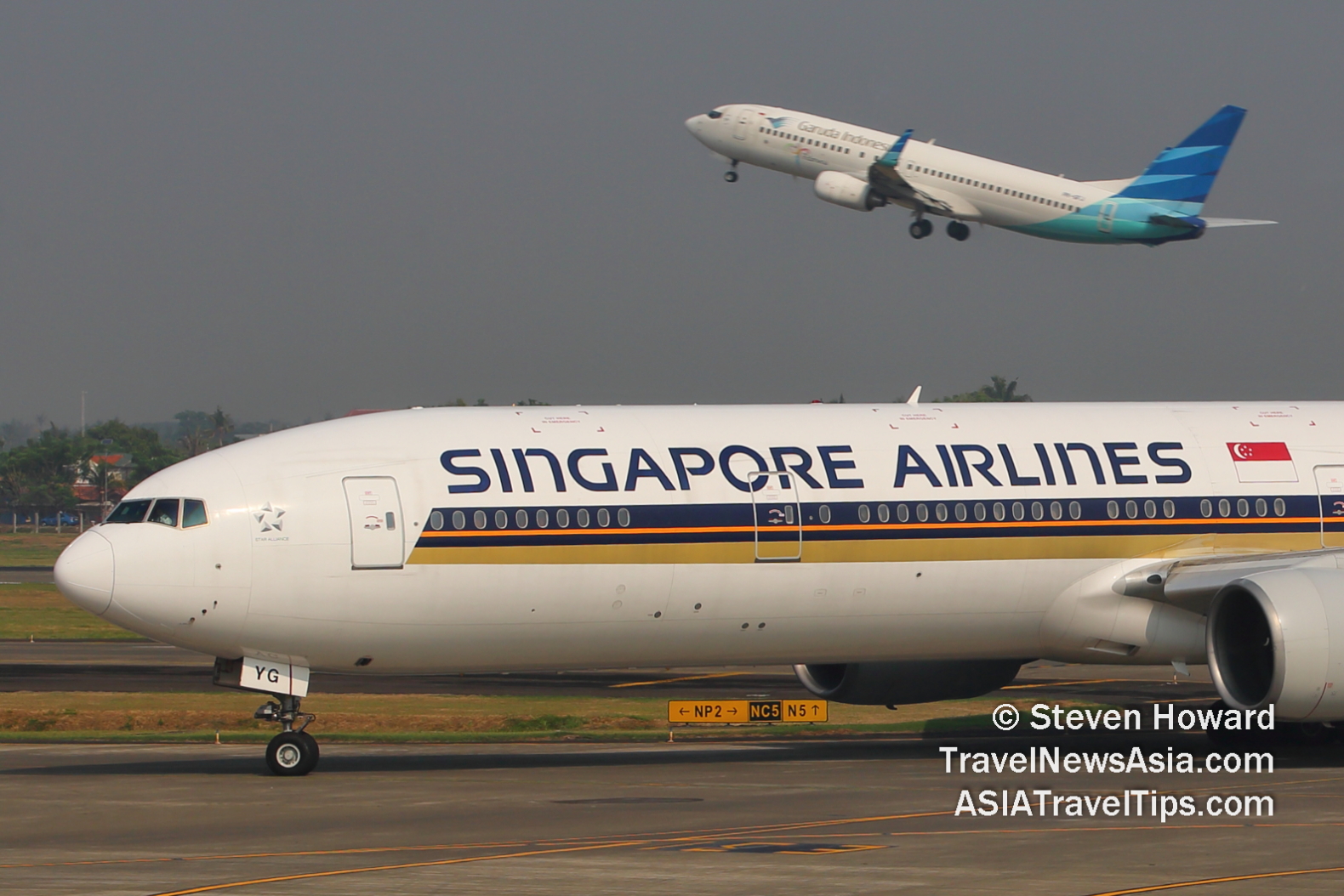 SIA B777 reg: 9V-SYG in the foreground with Garuda B737 taking off in the background. Picture by Steven Howard of TravelNewsAsia.com Click to enlarge.